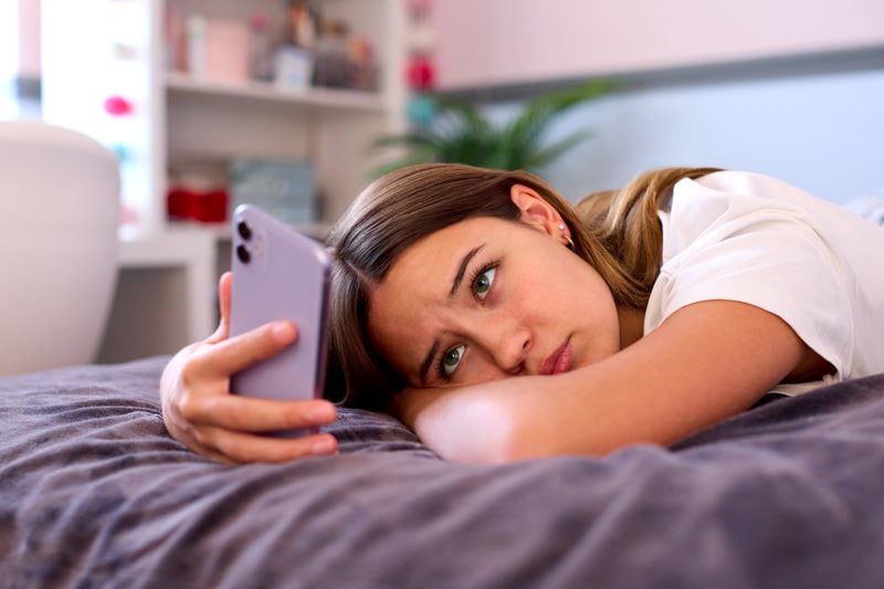 Photo of a teen girl looking at her iPhone unhappily